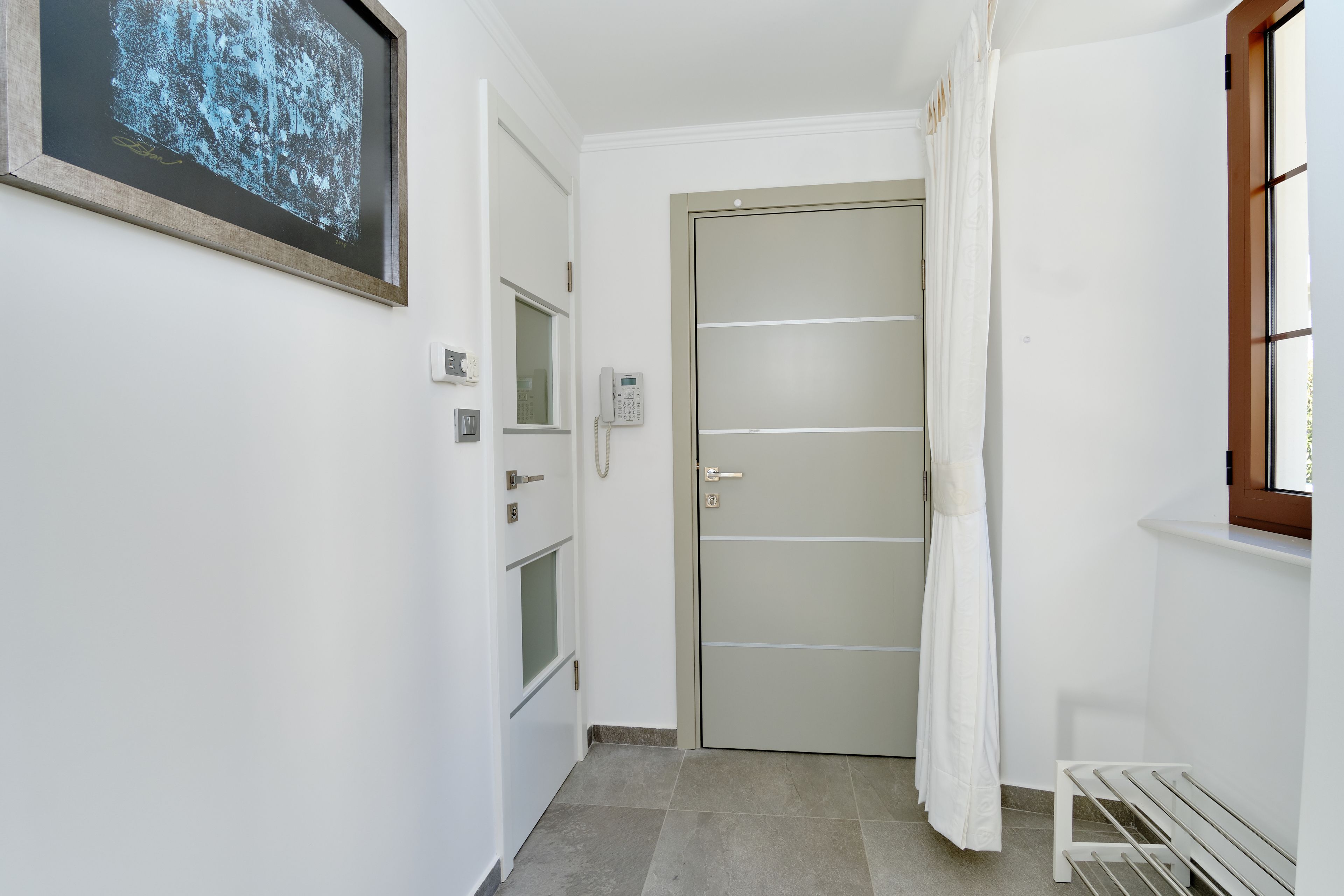 A narrow hallway with a door, a telephone, and a small bench.