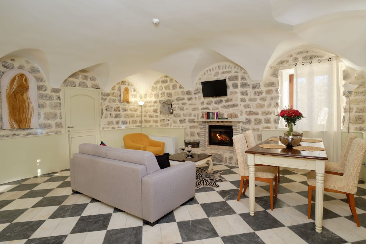 A living room with a checkered floor, a sofa, a table with chairs, a fireplace, and stone walls.