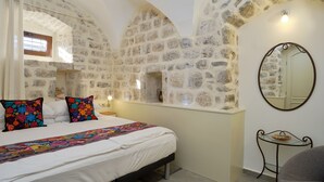 A bedroom with a stone wall, a bed with colorful pillows, a bedside table with a lamp, and a small table with a bowl. - Zebra  (Tivat)