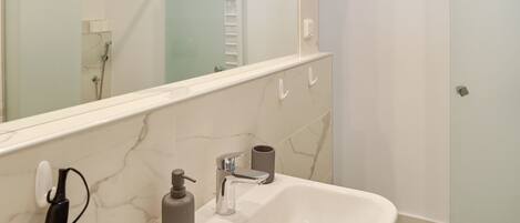 Un baño moderno con un lavamanos blanco, un espejo grande y una zona de ducha.