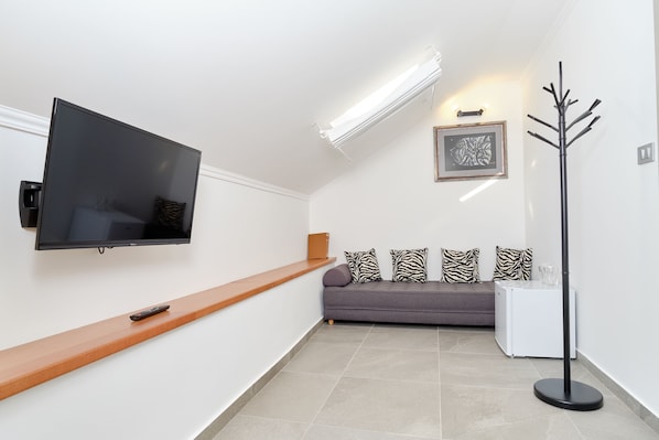 Un salon moderne avec un téléviseur à écran plat fixé au mur, un banc en bois, un canapé gris agrémenté de coussins à motifs, une lampe sur pied et un petit meuble blanc.
