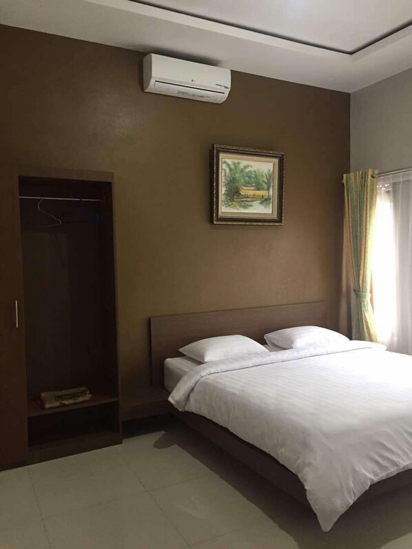 Una habitación de hotel con cama, armario, aire acondicionado y un cuadro en la pared.