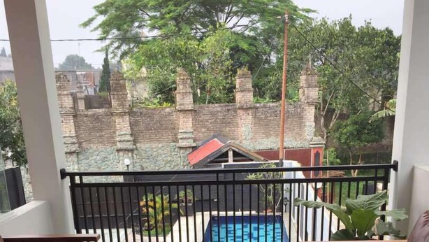 A balcony with a pool, wooden furniture, and a view of a stone wall and trees. - Villa Fahim 1 Puncak 4 Bedroom (Cipanas)