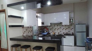 A modern kitchen with white cabinets, a black countertop, and a built-in island with bar stools. - Villa Fahim 1 Puncak 4 Bedroom (Cipanas)