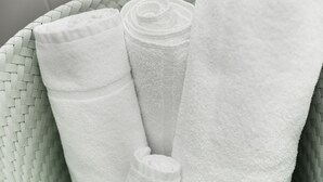 A woven basket containing neatly rolled white towels. - Dom Studios (St. Gallen)