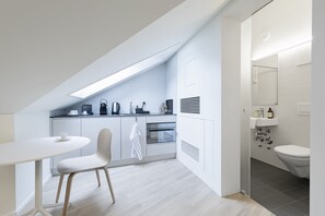Une cuisine moderne avec un coin repas, un four encastré et une salle de bain séparée, équipée de toilettes et d’un lavabo.