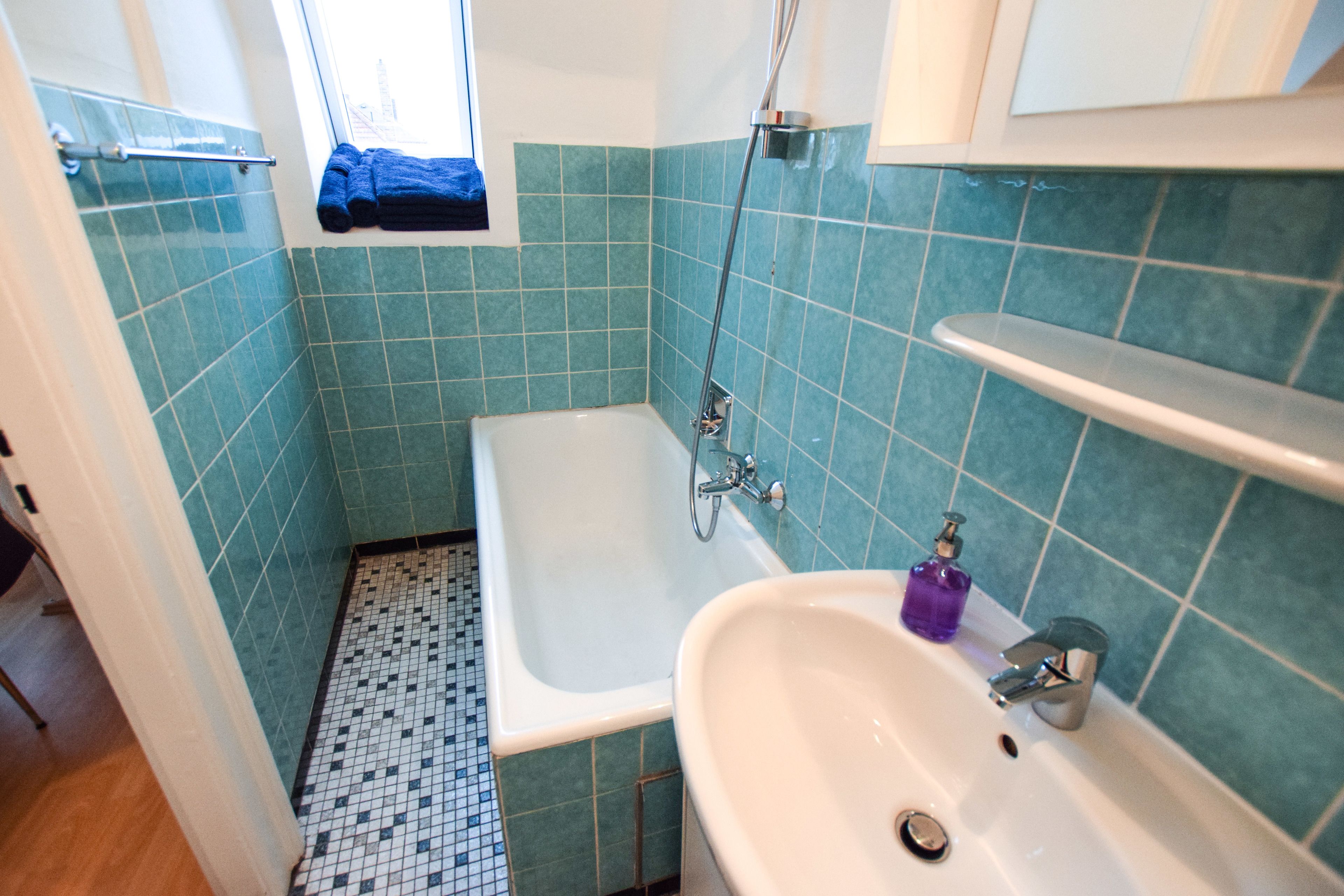 Un bagno con una vasca da bagno bianca, un lavandino con un erogatore di sapone viola e una finestra con porta asciugamani.