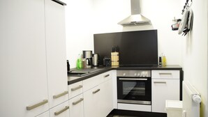 Ett modernt kök med vita skåp, en svart bänkskiva och rostfria köksmaskiner, inklusive en ugn och en kaffebryggare.