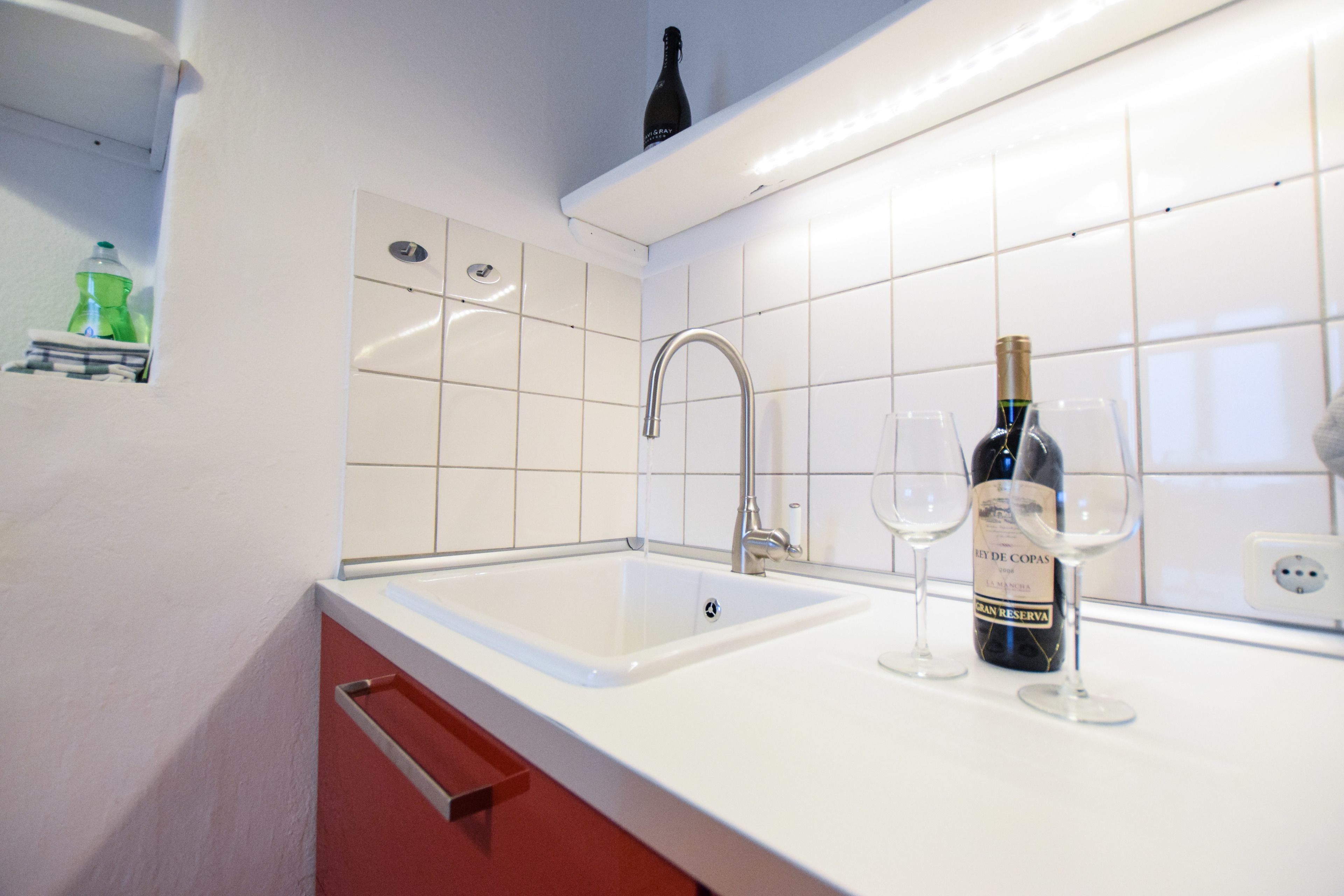 A kitchen with a white sink, stainless steel faucet, and a wine bottle on the counter.