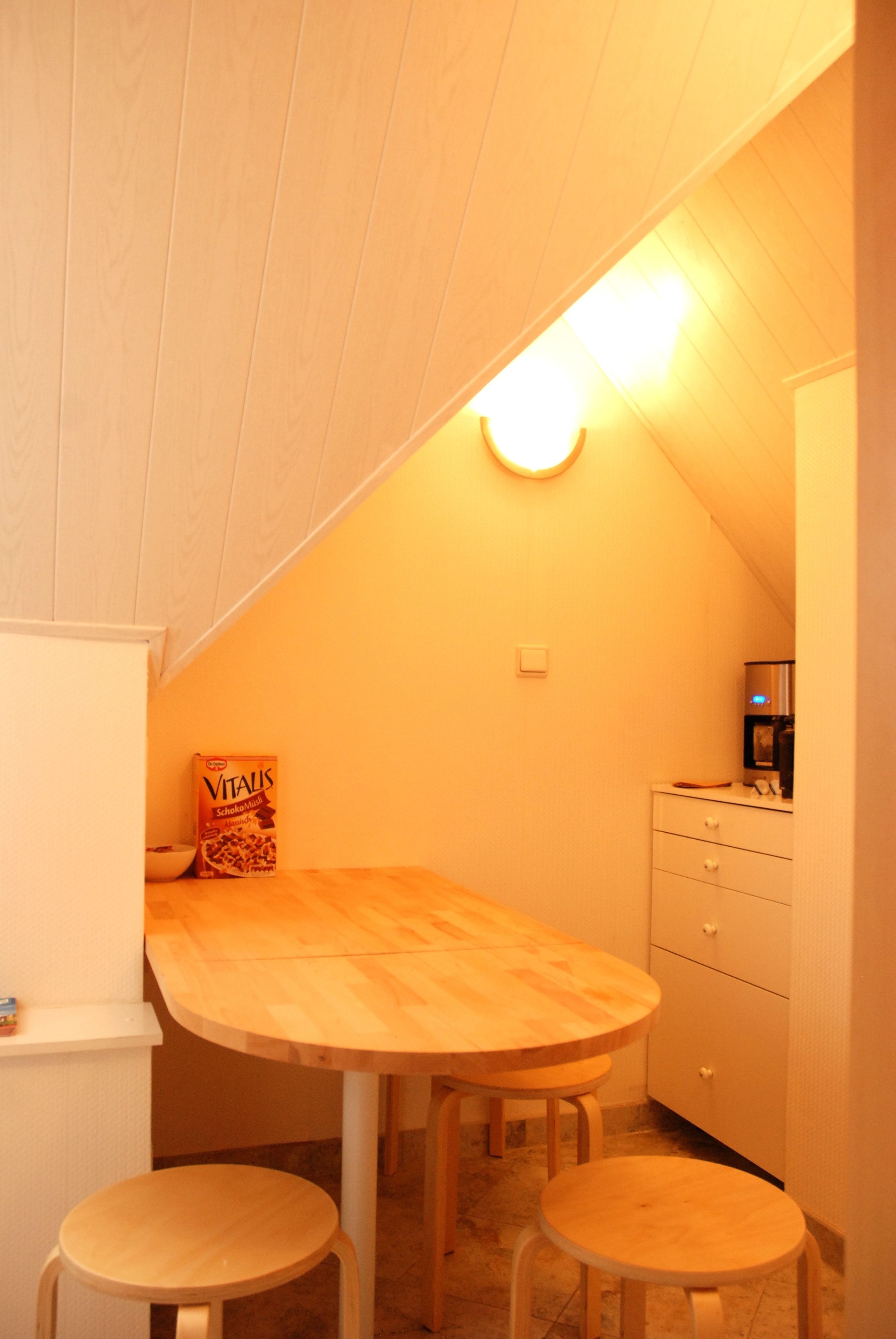 A small kitchen with a wooden table and stools, a box of cereal, and a coffee machine.