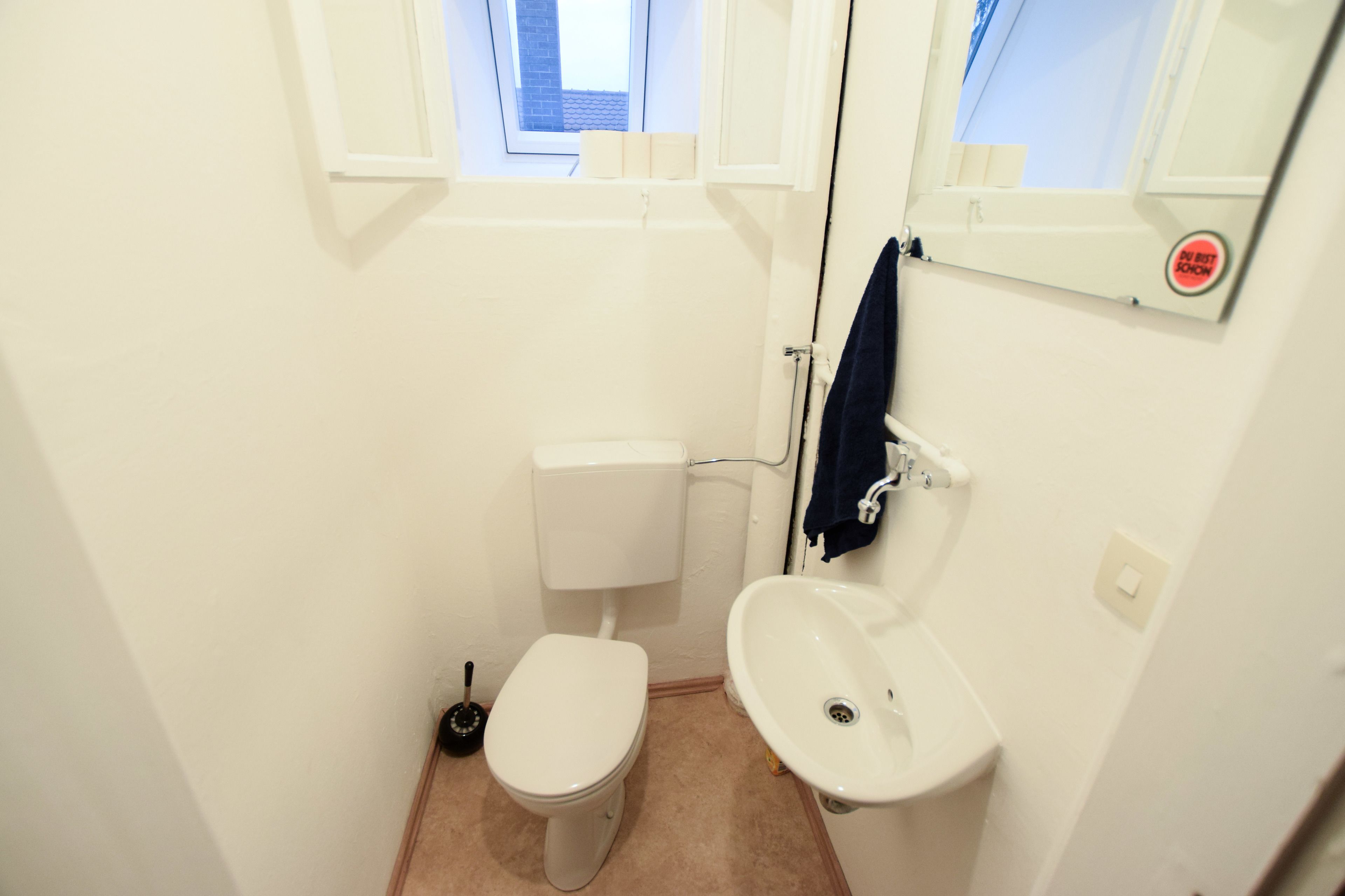 Une petite salle de bain blanche, avec des toilettes, un lavabo et une fenêtre.