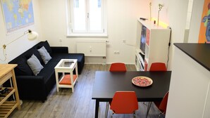 Ett kompakt vardagsrum med en svart soffa, ett litet vitt bord, ett svart matbord med röda stolar, ett vitt skåp och en världskarta på väggen.