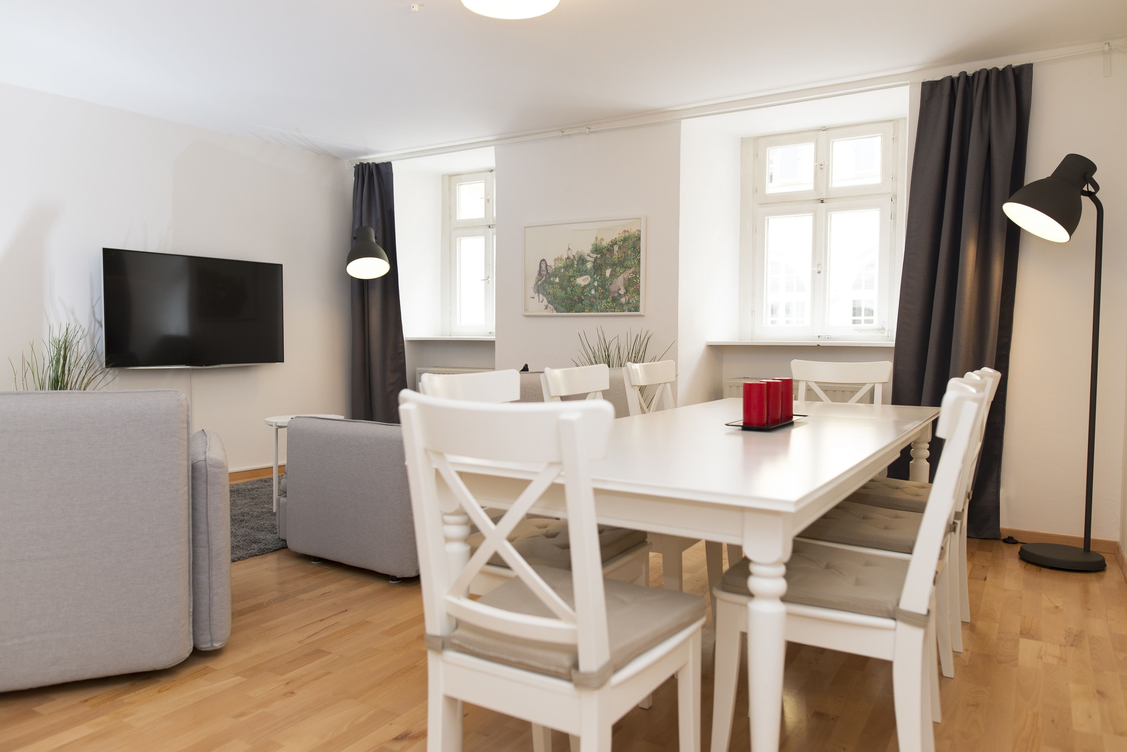 A modern living room with a flat-screen TV, white furniture, and a painting on the wall.