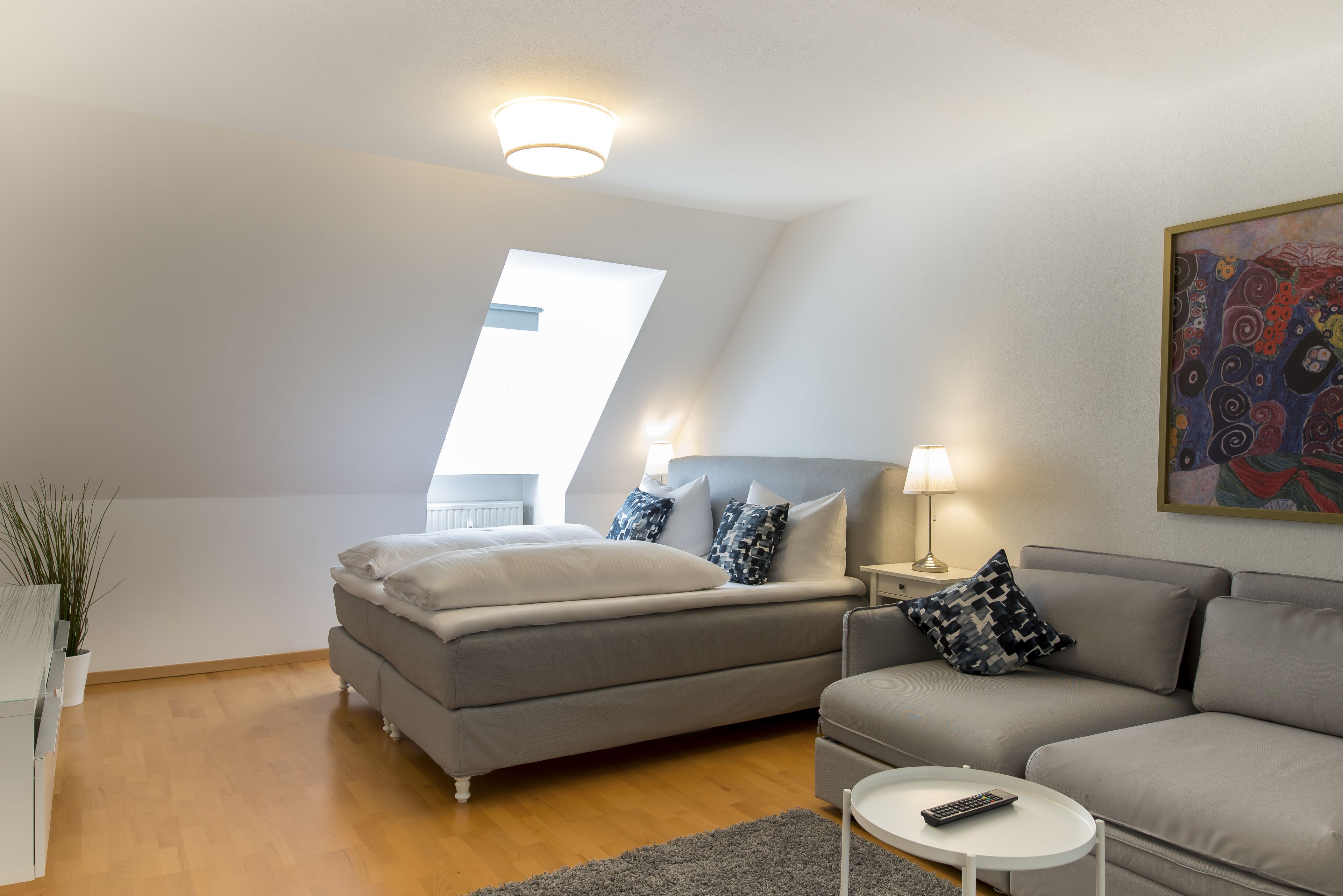 Ein modernes Schlafzimmer mit einem Bett, einem grauen Sofa, einem kleinen Tisch und einem Nachttisch.