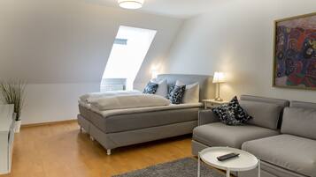 Ein modernes Schlafzimmer mit einem Bett, einem grauen Sofa, einem kleinen Tisch und einem Nachttisch.