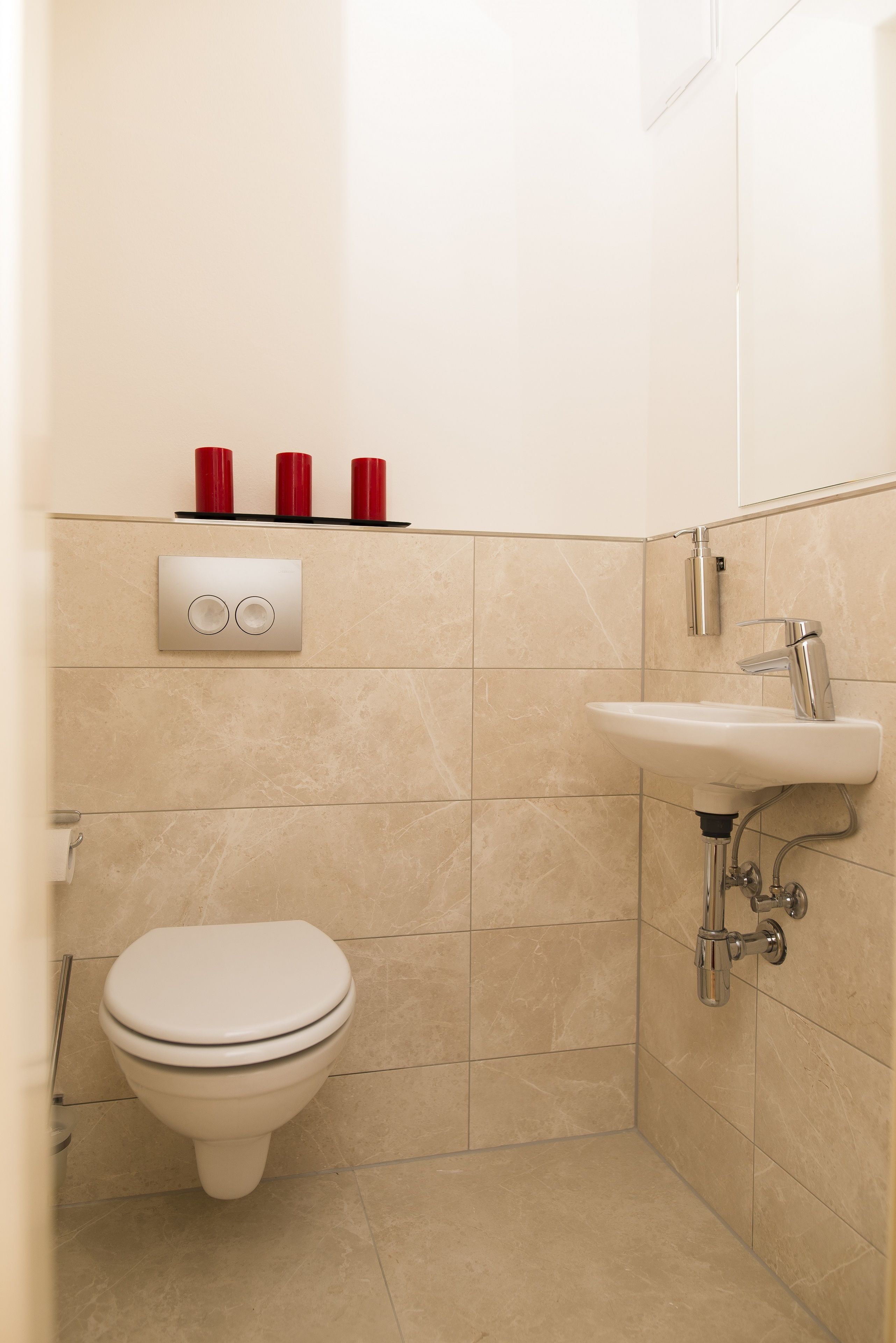 Ein Badezimmer mit Toilette, Waschbecken und drei roten Tassen auf einem Regal.
