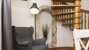 Canto de um quarto com uma poltrona cinza, uma escada espiral de madeira e um vaso de planta.