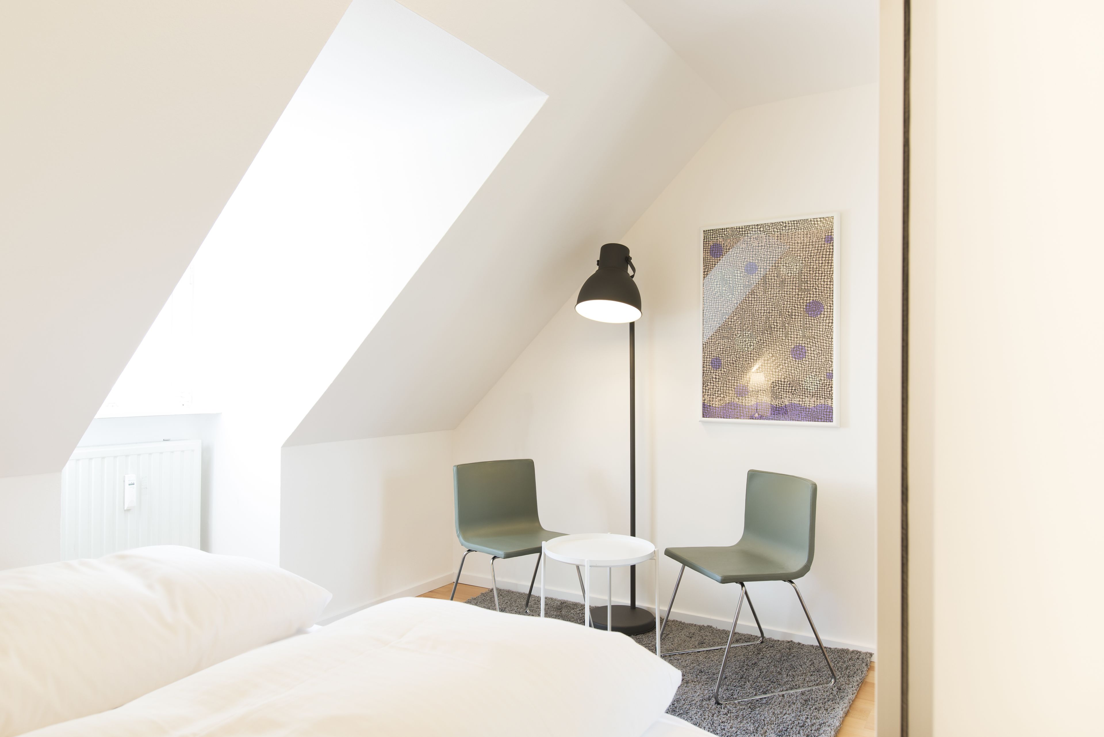Ein modernes Schlafzimmer mit Dachfenster, einem Bett, zwei Stühlen, einem kleinen Tisch und einer Stehlampe.