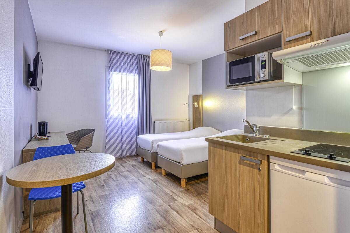 Una habitación de hotel compacta con kitchenette, una cama, una pequeña mesa de comedor y un televisor.