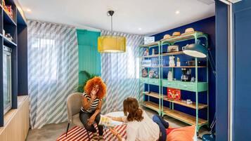 Een kamer met een muur in teal, een gestreept gordijn, een groen metalen rek met het opschrift 'BIBLIOTHEEK' en een rood-wit gestreept vloerkleed.