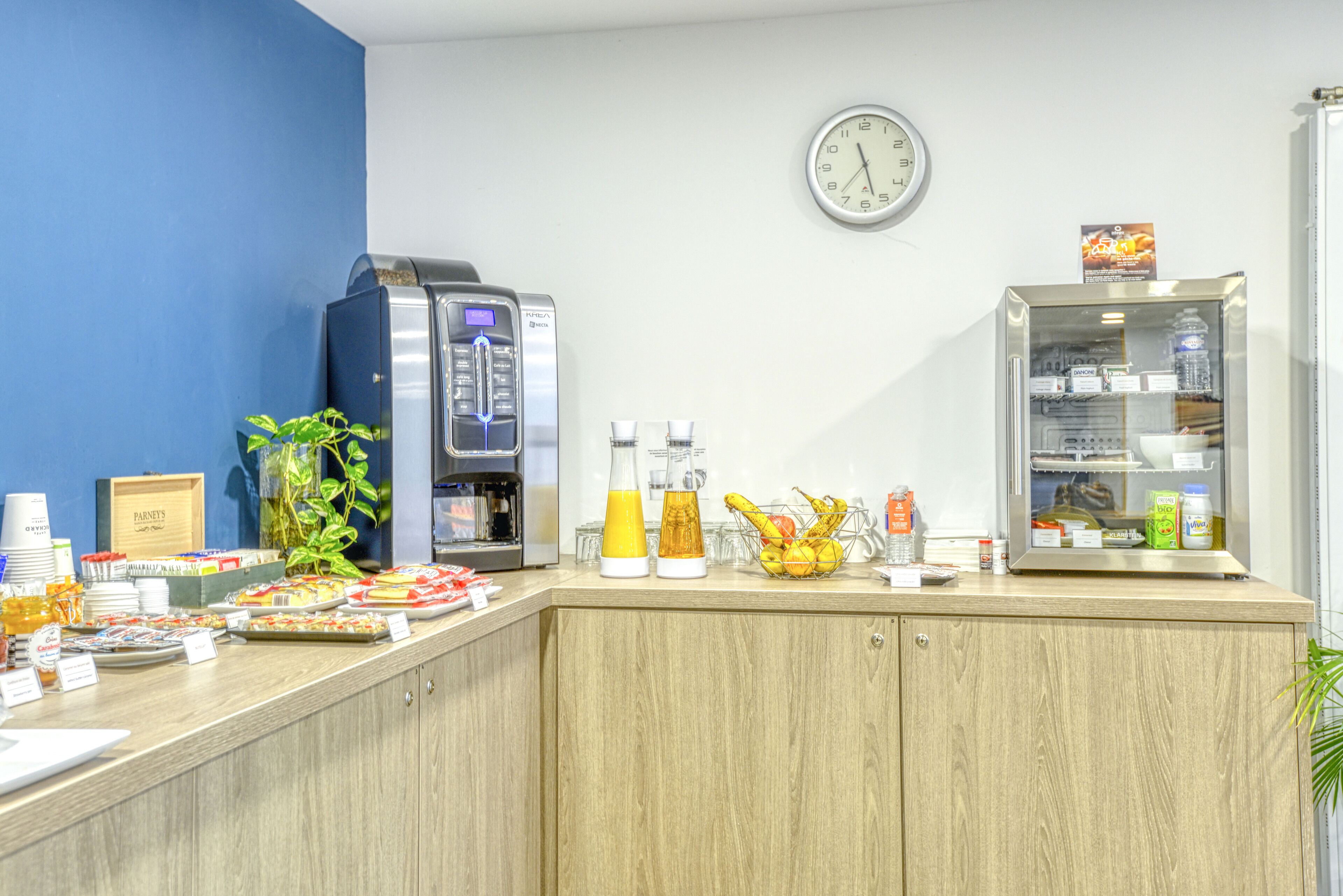 Una barra de desayuno con máquinas de café, dispensadores de zumo y un refrigerador lleno de bebidas.