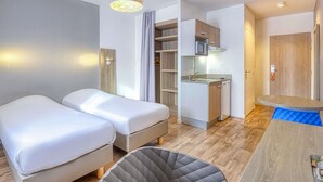 Een compacte hotelkamer met twee bedden, een kitchenette, een kleine eethoek en een badkamer.