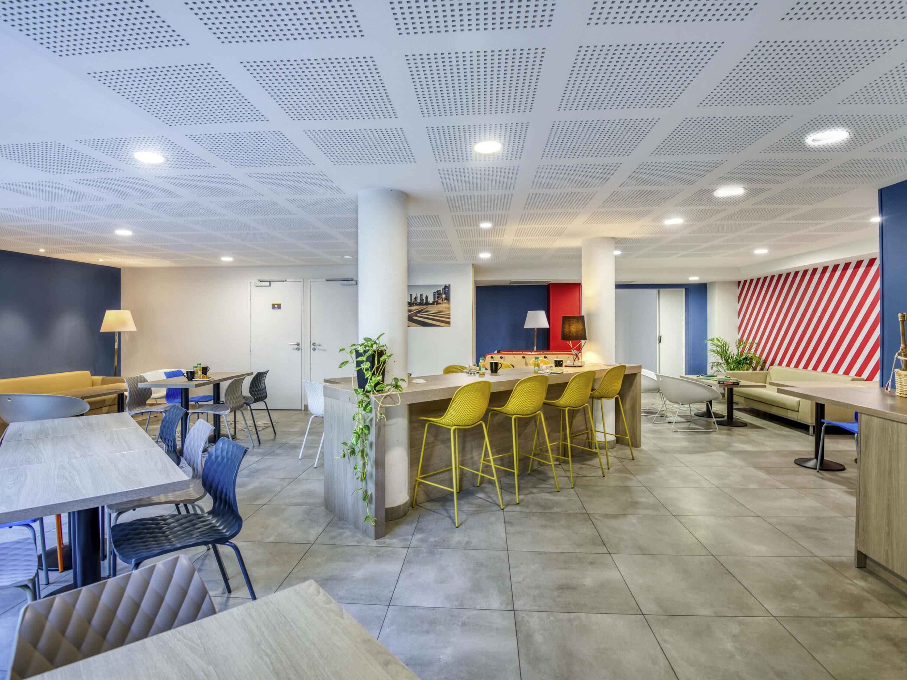 A modern hotel lobby with a central bar area, seating arrangements, and a large window.