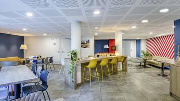 En modern hotellobby med en central bardisk, sittgrupper och ett stort fönster.