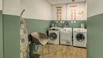 A laundry room with two washing machines, a drying rack, and instructional posters on the wall.