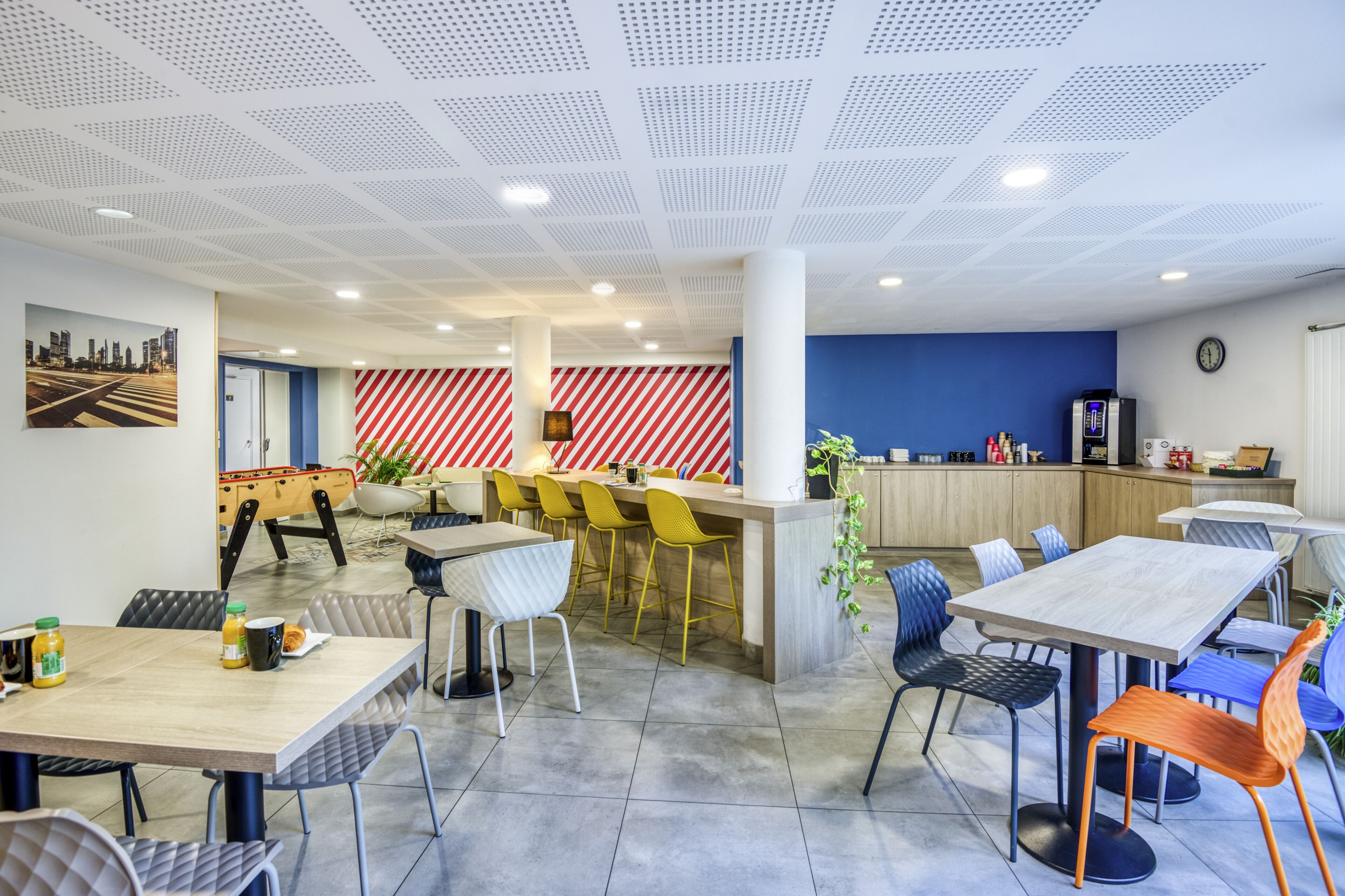 A modern dining area with a bar, seating arrangements, and a cityscape artwork on the wall.