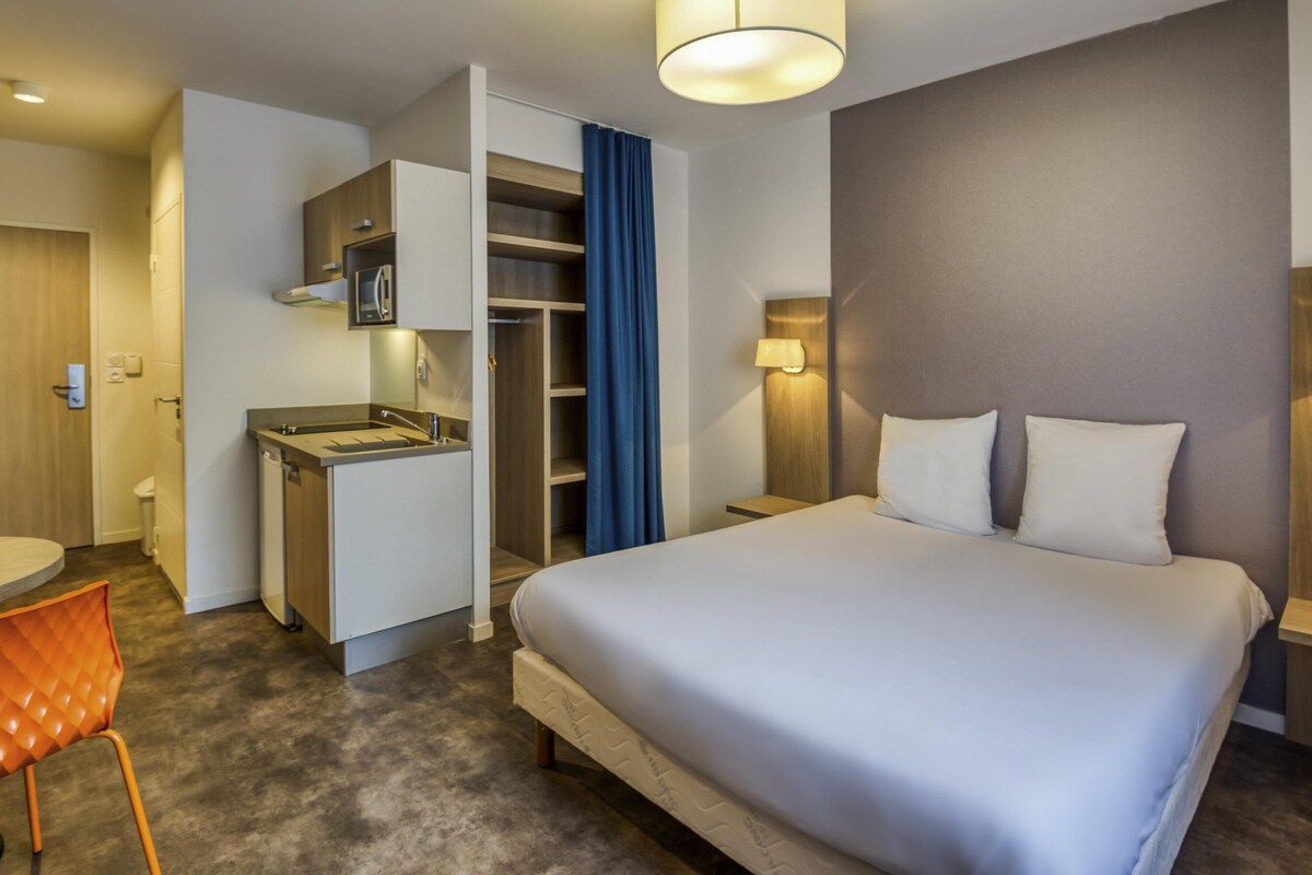 A hotel room with a bed, a desk, a chair, a wardrobe, and a bathroom.