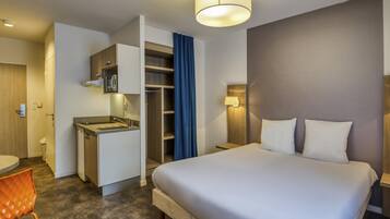 Une chambre d’hôtel comprenant un lit, un bureau, une chaise, une armoire et une salle de bain.
