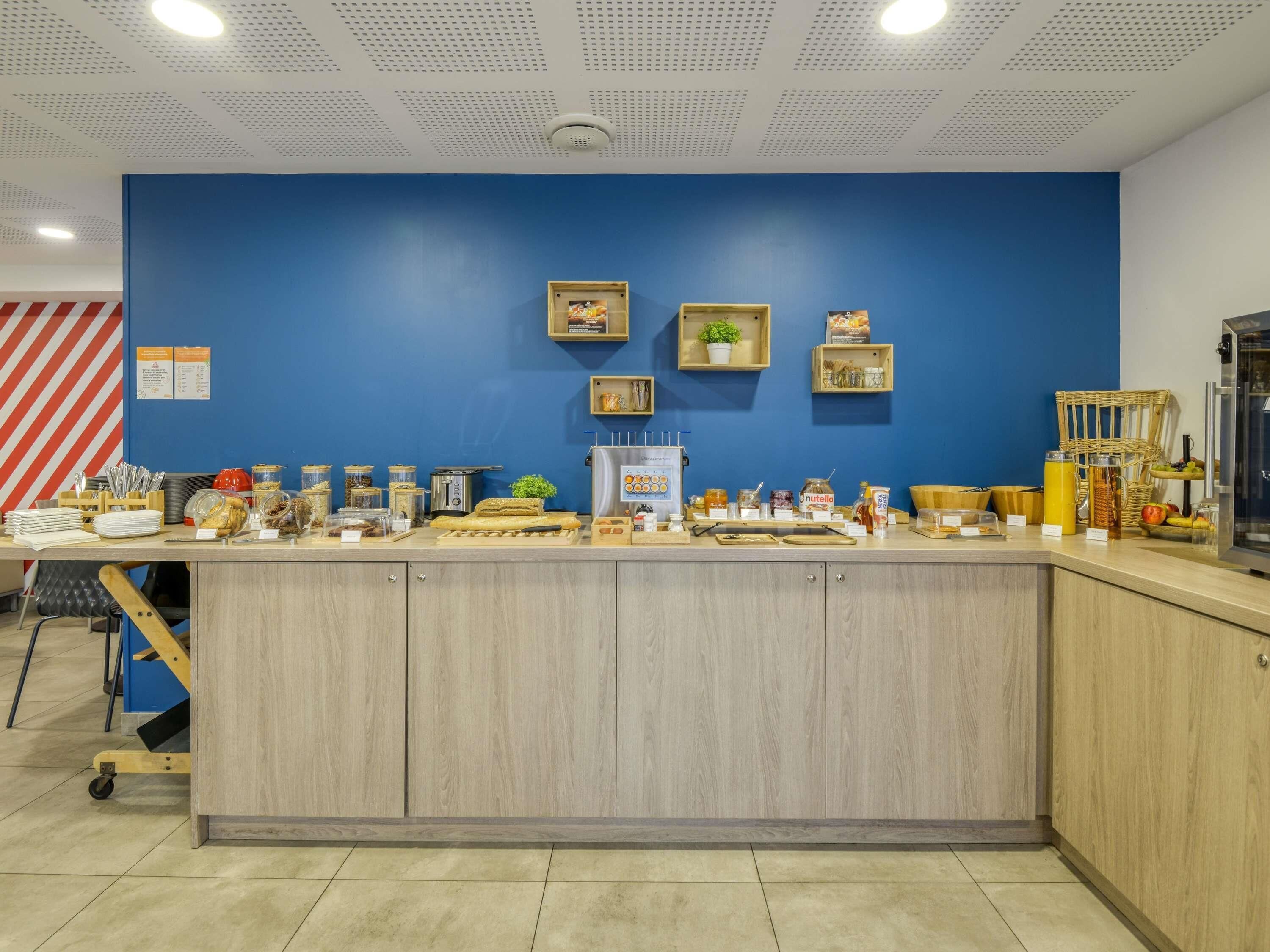 A breakfast bar with various food items and condiments, a coffee machine, and a small plant on the wall.