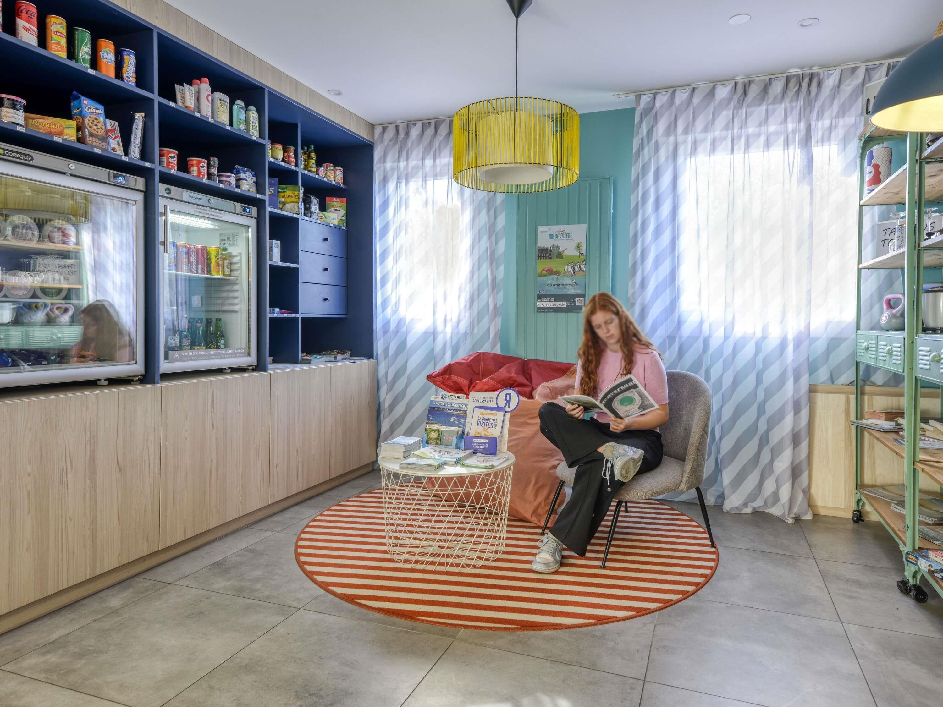 Una habitación con zona de estar, un refrigerador lleno de comida y una ventana con cortinas.