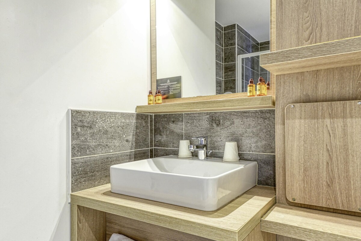 A modern bathroom with a white sink, wooden vanity, and a mirror above the sink.