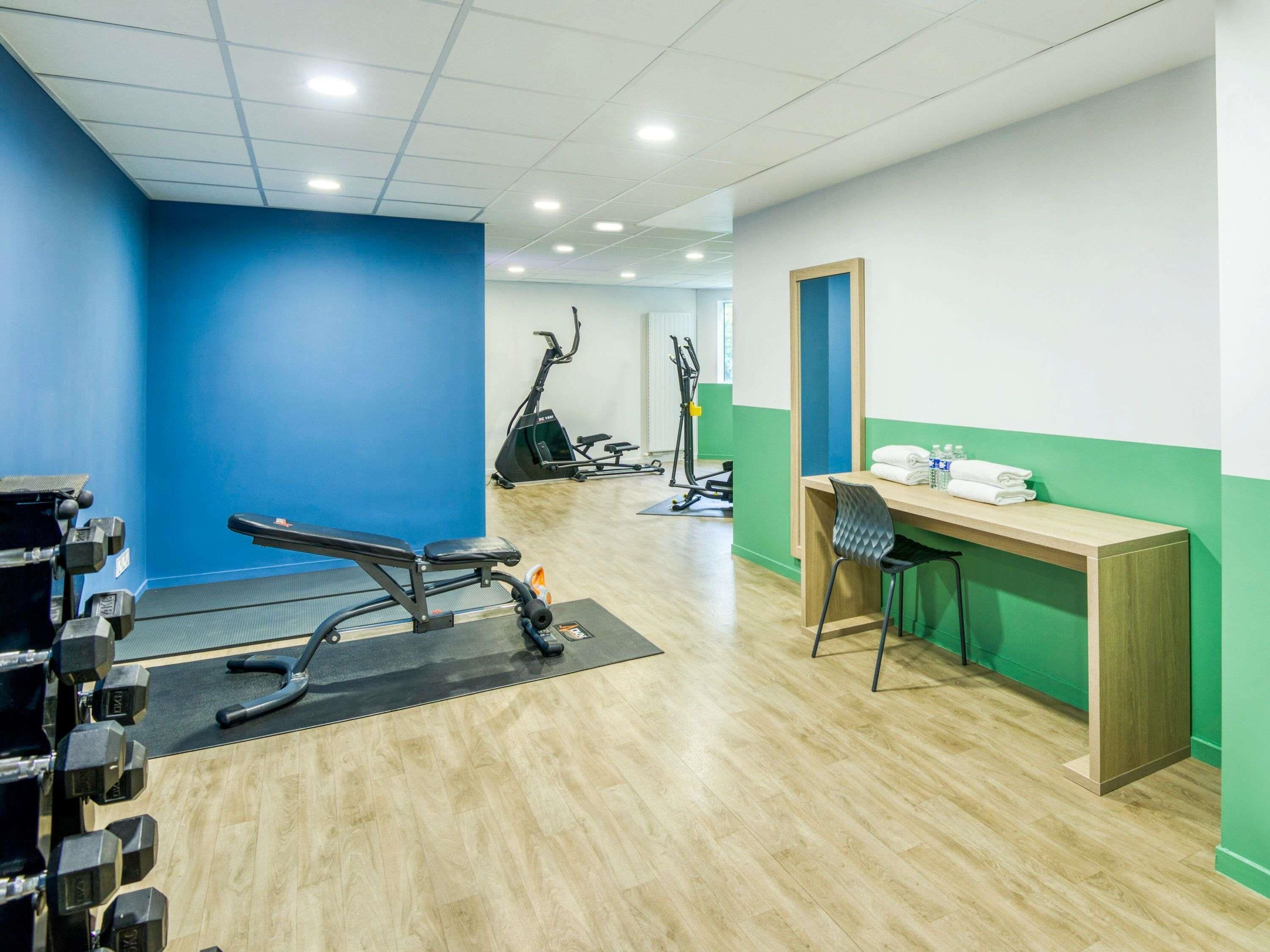 Een sportschool met trainingsapparatuur, een bureau met stoel en een spiegel aan de muur.