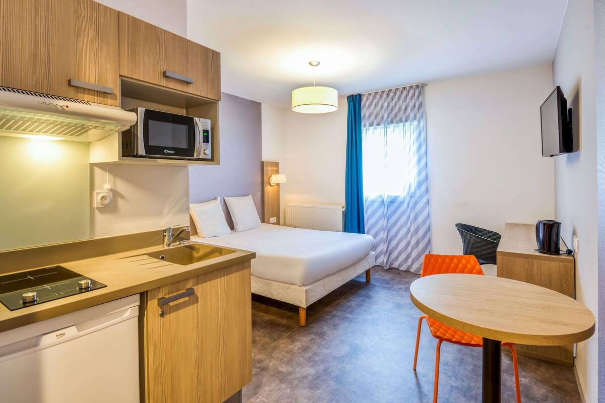 Habitación de hotel con kitchenette, cama, mesa de comedor y televisor.
