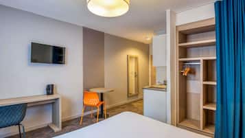 Une chambre d’hôtel comprenant un lit, un bureau, une chaise, une télévision, un miroir, une armoire et une salle de bain avec un lavabo et un miroir.