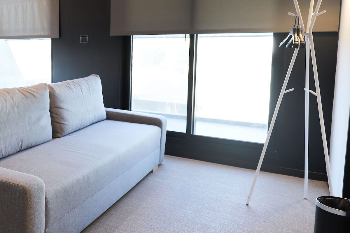 A hotel room with a bed, a grey sofa, a TV, and a window with a view.