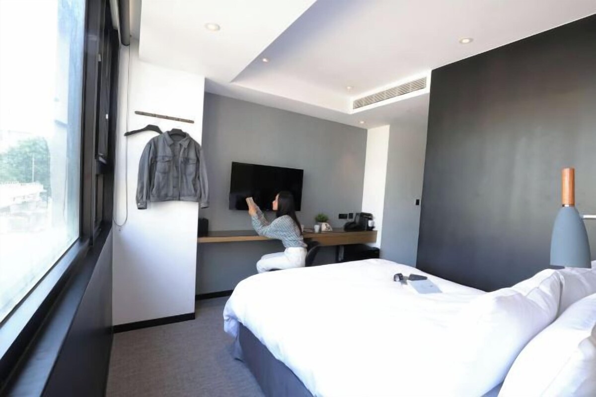 Una habitación de hotel moderna con una cama grande, un escritorio con televisor de pantalla plana y una ventana que ofrece vistas al exterior.