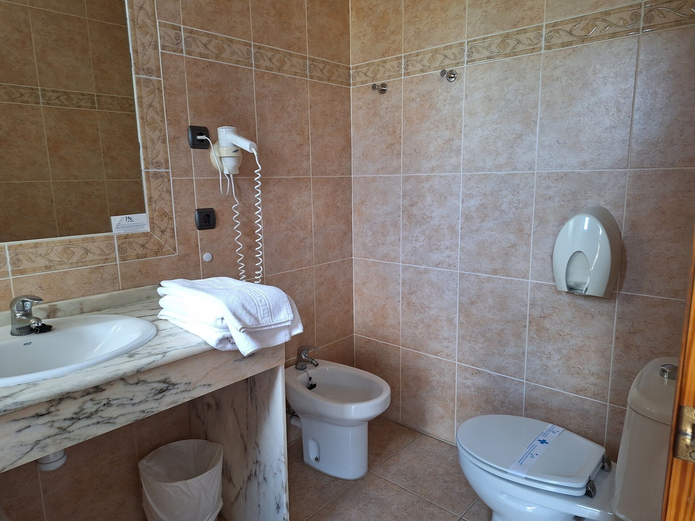 Un baño con lavamanos de mármol, inodoro blanco, bidé y secador de pelo en la pared.