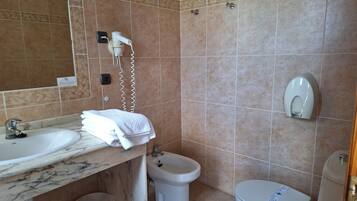 A bathroom with a marble sink, a white toilet, a bidet, and a hairdryer on the wall.