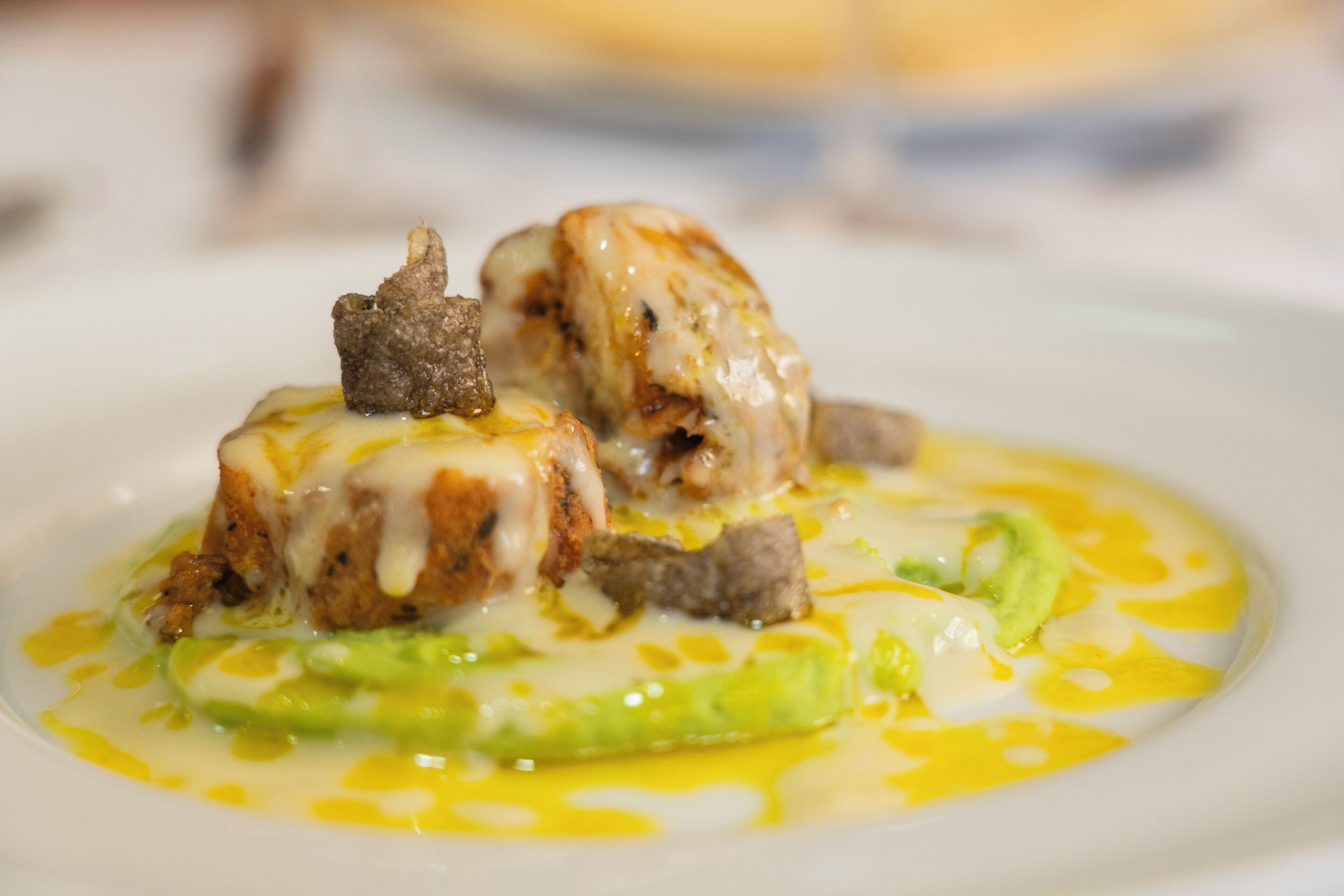 Un plato de comida con salsa cremosa, verduras verdes y un trozo de carne.