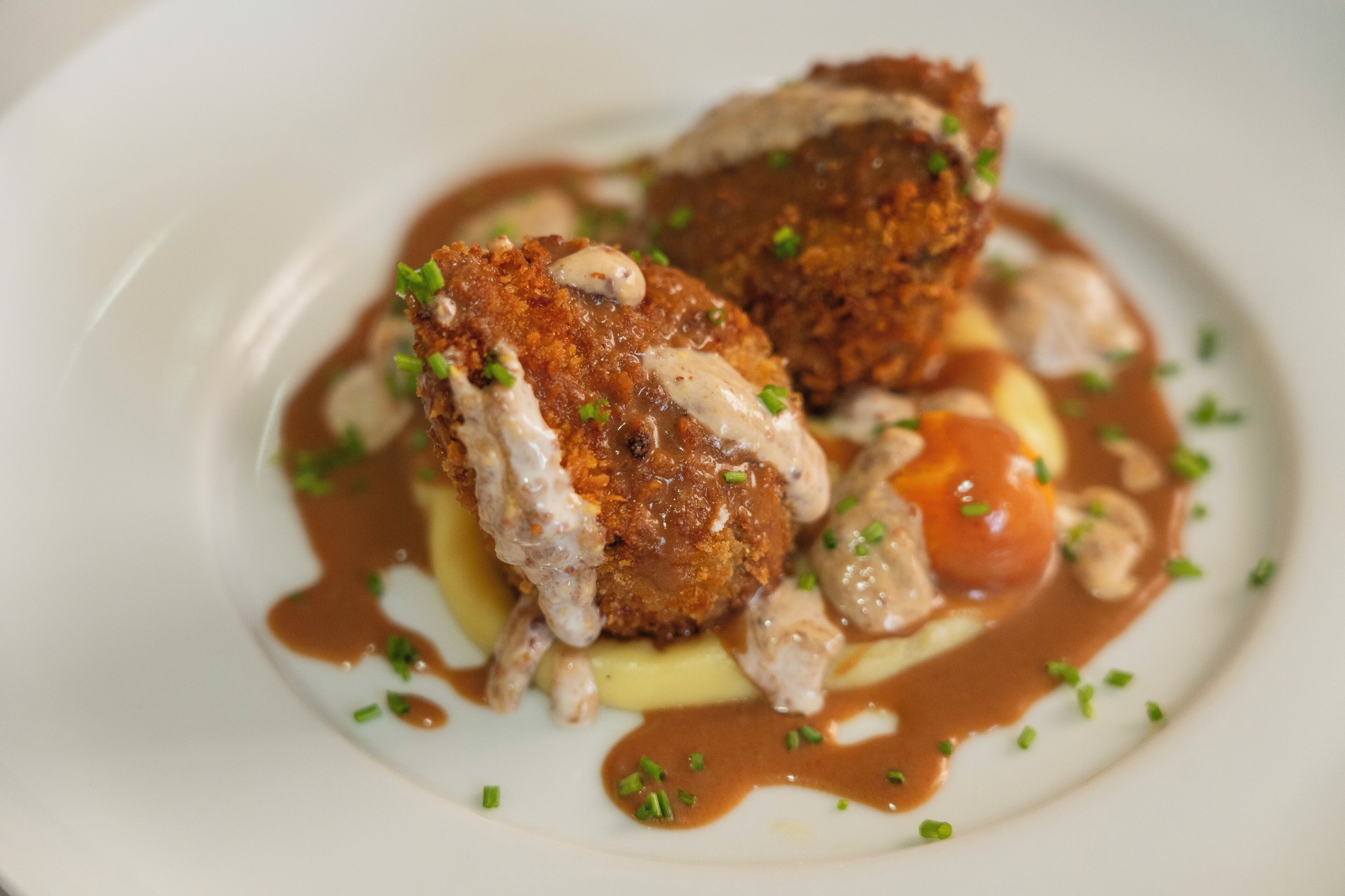 A dish with breaded meat, sauce, and garnishes on a plate.
