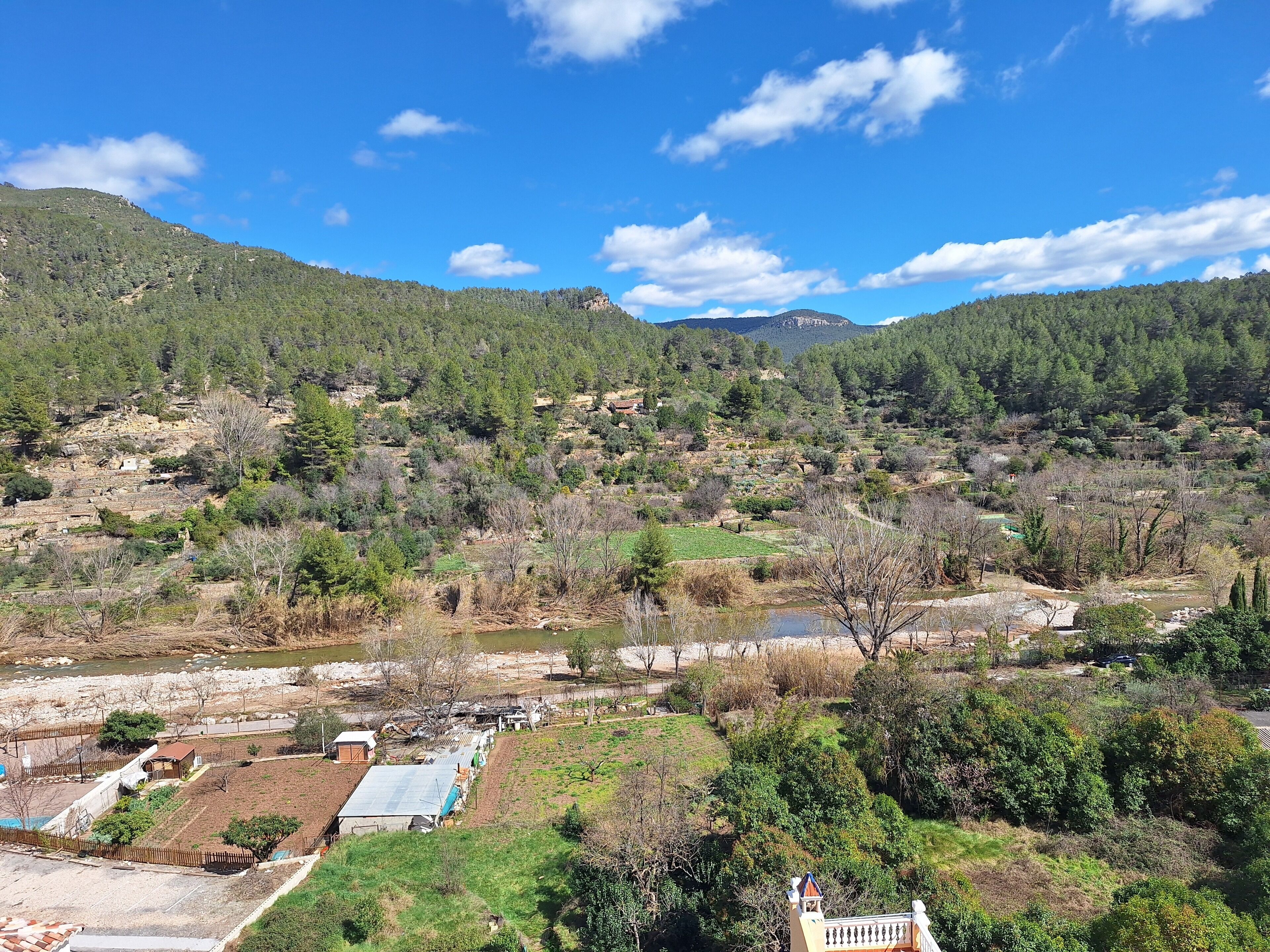 A rural landscape with a river, terraced fields, and a small building with a blue roof.