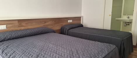 A room with two beds, a wooden headboard, a white wall, and a bathroom visible through an open door.