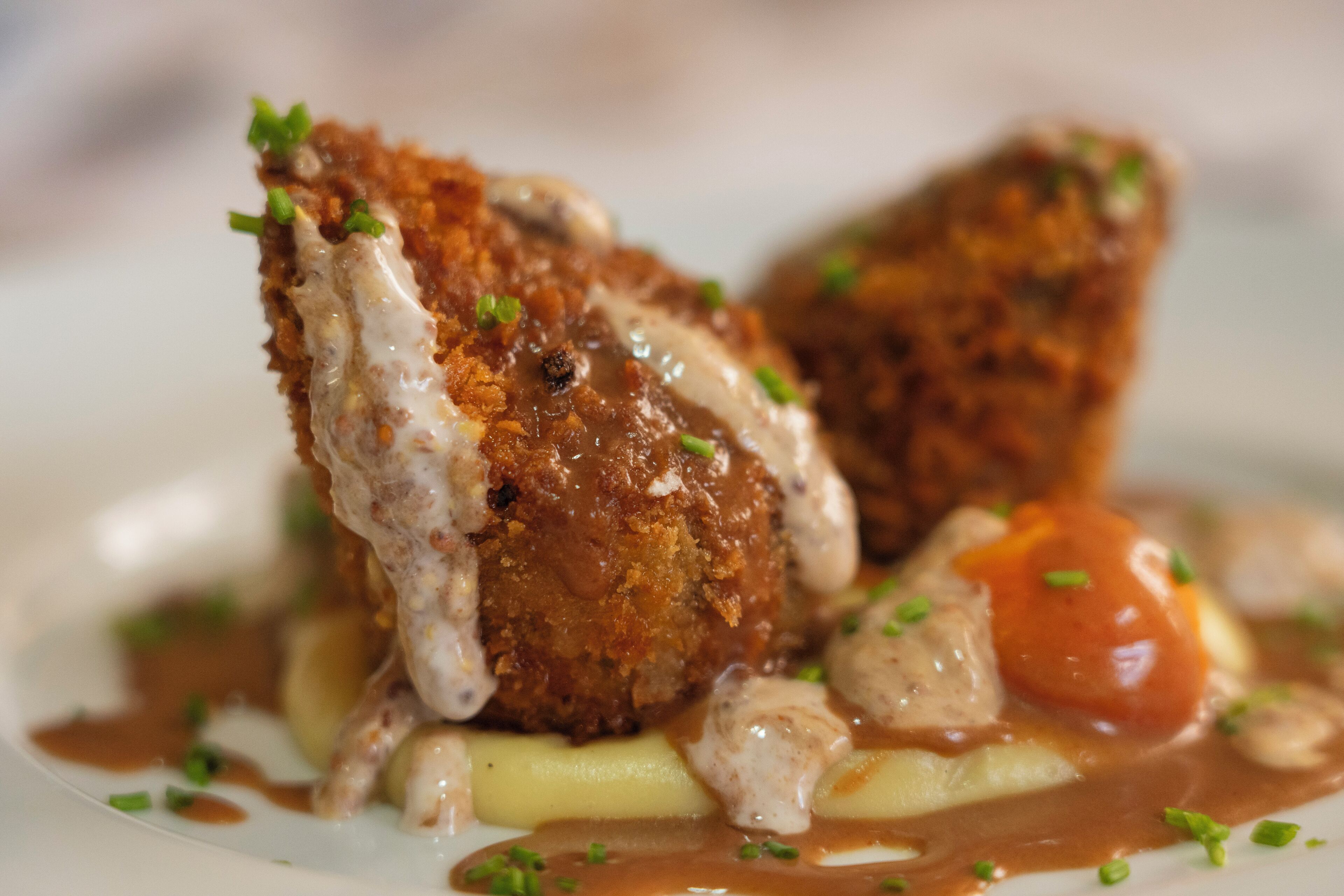 A plated dish with breaded chicken, mashed potatoes, and a creamy sauce, garnished with herbs.