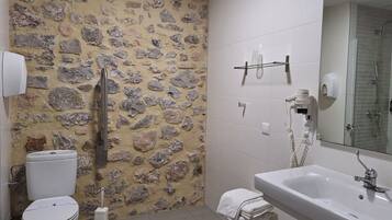 Et badeværelse med stenvæg, toilet, håndvask og brusebad.