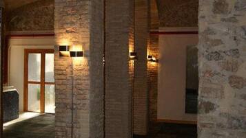 An interior with stone arches, a tiled floor, and wall-mounted lights.