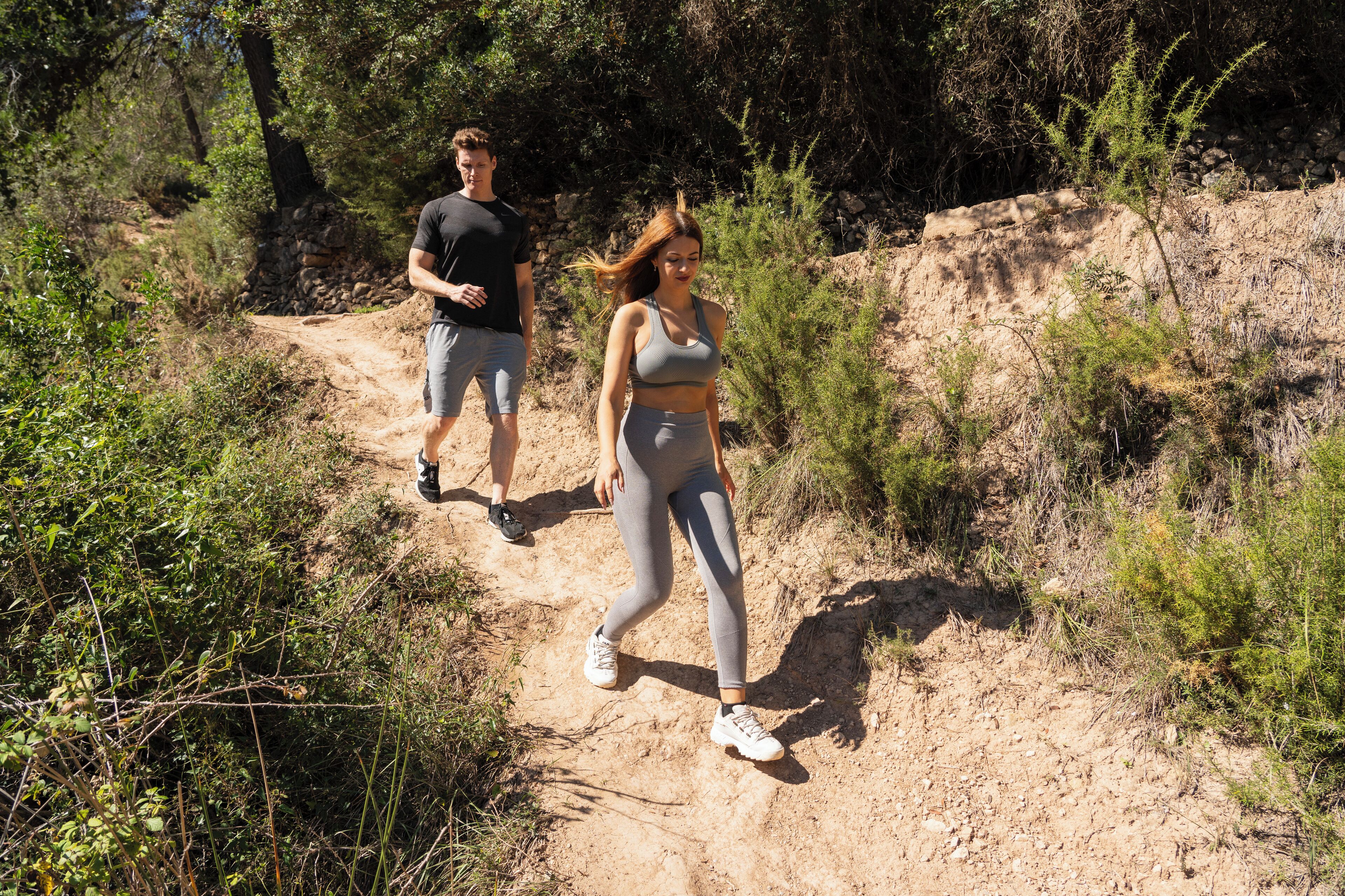 Dos personas caminando por un sendero de tierra rodeado de vegetación.